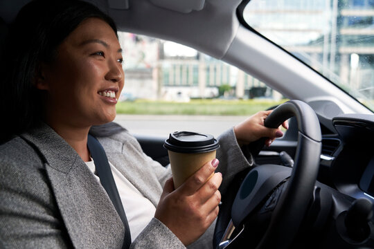 Chinese woman driving a car and holding a cup of coffee