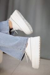TThe legs of a teenager in light jeans and fashionable white sneakers on a platform on a light blue fabric background. High quality photo