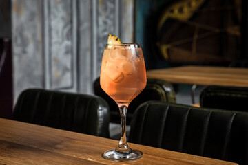 A cold refreshing low abv cocktail served in a wine glass with ice cubes garnished with dried pineapple slice on a wooden table at the bar or restaurant