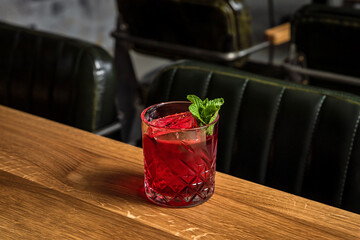 A red alcoholic cocktail in a rocks glass served on ice and garnished with mint - 608136544