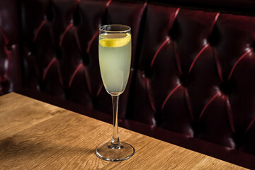 French 75 cocktail made of gin, lemon juice, sugar simple syrup, prosecco sparkling wine served in a flute glass garnished with lemon twist, on a wooden table in restaurant or bar, horizontal photo