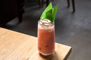 A sweet cold low abv tropical refreshing cocktail in a highball glass served on ice garnished with dried coconut and banana leaf