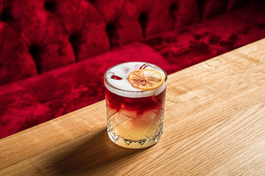 New York sour or Continental sour cocktail with bourbon or whisky garnished with dried lemon wheel at the wooden table at bar or restaurant, horizontal photo