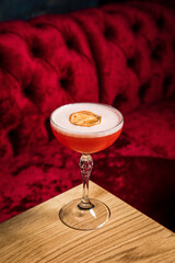 A pink sour alcoholic cocktail with foam garnished with dried lemon wheel served in a coupe glass on a wooden table of restaurant or bar - 608138599