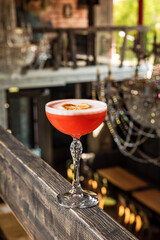 A pink sour alcoholic cocktail with foam garnished with dried lemon wheel served in a coupe glass in a restaurant or bar