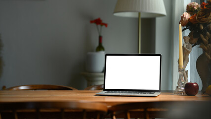 Comfortable home interior with laptop computer, candle holder, beautiful roses in ceramic vase on wooden table