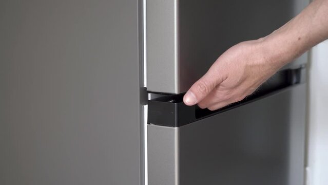 open the fridge,a man opens a gray refrigerator with his hand