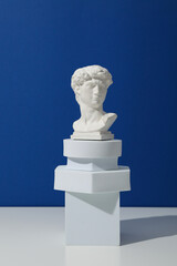 Obraz premium Geometric figures and ancient head on white table against blue background