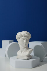 Geometric figures and ancient head on white table against blue background