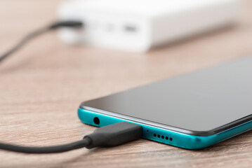 Charging phone via usb cable, powerbank on the background. Using power bank for charging devices concept