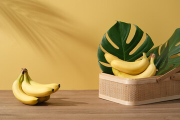 Background with minimalist style for product brand presentation and copy space - Fresh bananas on bamboo basket with monstera leaves on wooden table on yellow background with palm leaf shadow © Tuan  Nguyen 