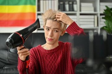A professional young Asian gay beauty blogger using a hairdryer and filming his hair style tutorial