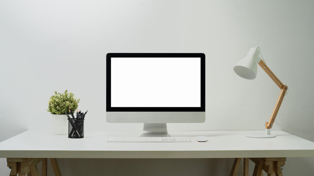 Blank screen computer, lamp, pencil holder and potted plant on white table. Empty screen for your webpage or advertise text