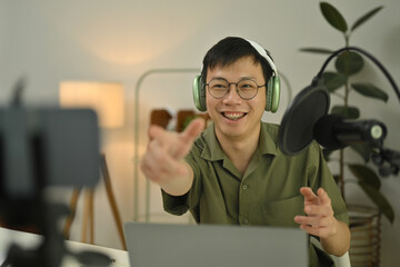 Cheerful man radio host in headphone using condenser microphone to recording podcast in small home...