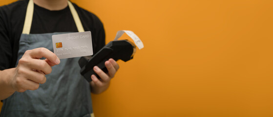 Unrecognizable holding credit card and payment terminal on yellow background. Electronic money,...