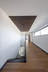 an empty corridor with white walls and a wooden staircase going down