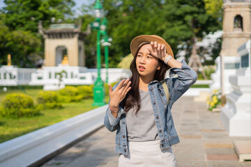 Portrait of Asian female traveler fanning and sweating on sidewalk of temple on street in Bangkok,...