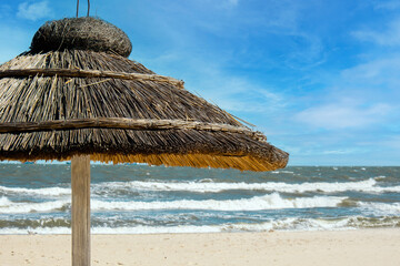 Straw beach rattan parasol at the empty beach with blue sky backgrounds sea ocean coast. Relaxing day. Copy space for your text. Idyllic travel and summer vacation concept. Straw umbrella on beautiful