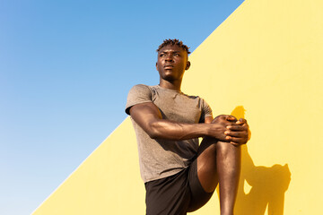 Young man doing stretching exercise outside. African man training outside.. - Powered by Adobe