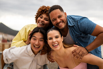 A group of multi-ethnic young people happily have fun on an outdoor terrace.The Korean boy and the caucasian girl grab the African-American couple from behind.Concept of friends having multiracial fun