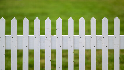 White rustic picket fence in front of green grass