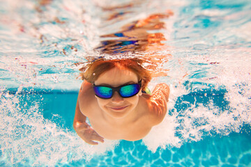 Summer child boy relax at aquapark. Summertime vacation. Little kid swim underwater in pool. Kid wearing summer goggles swims under water in poolside. Underwater photo.