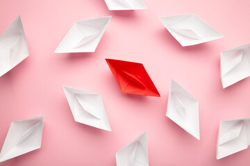 Leadership concept. Red leader paper ship leading among white on pink background.