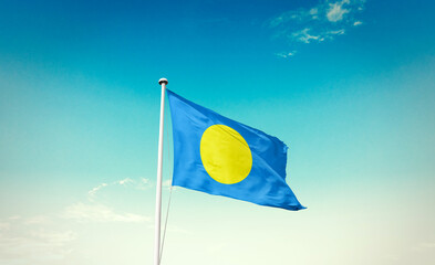 Waving Flag of Palau in Blue Sky. The symbol of the state on wavy cotton fabric.