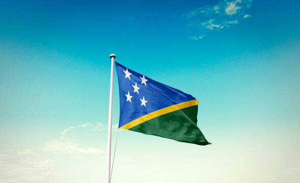 Waving Flag of Solomon Islands in Blue Sky. The symbol of the state on wavy cotton fabric.