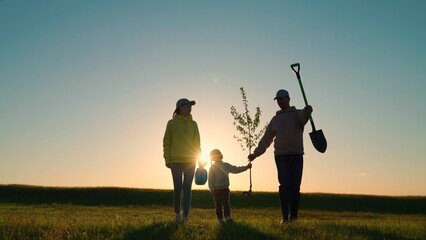 Happy family and child, team planting trees in spring. Silhouette of family with tree. Dad is...