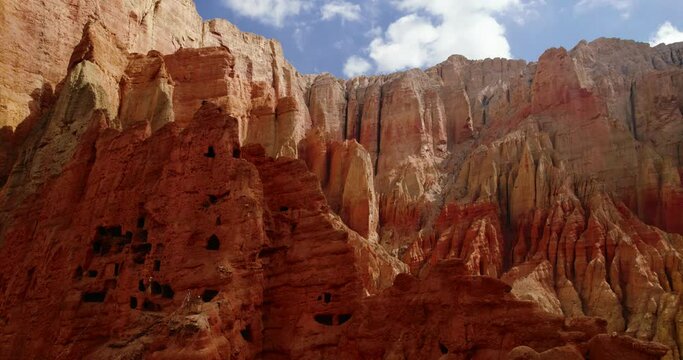 Drone explores unique red-orange cave-like structure in dry mountains of Dhakmar Village, Upper Mustang, Nepal. Alluring video showcases detailed landscape and artistic formations in Annapurna Area.
