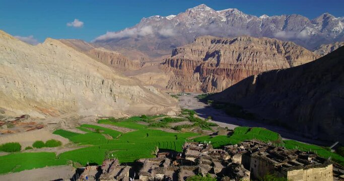 Drone shot captures beautiful Chusang village in Upper Mustang, Nepal. Unique structured dry mountains, snowy peaks, and a captivating blue sky backdrop. Explore the allure of Annapurna Area.