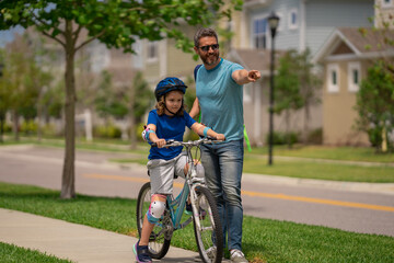 Father and son in bike helmet learning ride bicycle. Father and son on bicycle on summer day outdoor. Little son trying to ride bicycle with father. Fathers day. Childhood and fatherhood. Child care.