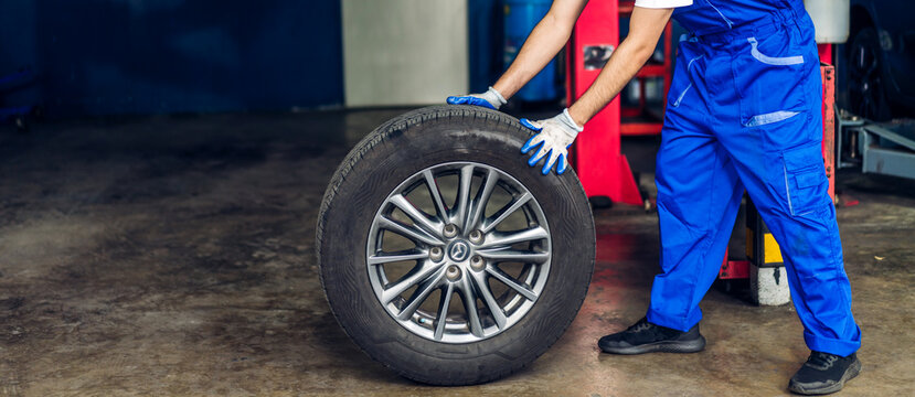 Professional car technician mechanic man in uniform work and maintenance repairing checking removing black wheel tire car before a long travel in auto service.Automobile service garage