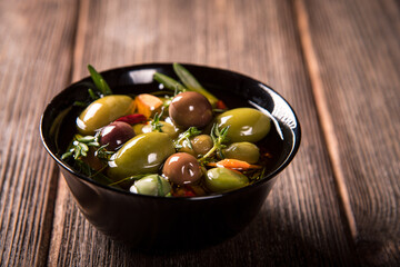 Olives in a black bowl on a wooden table.