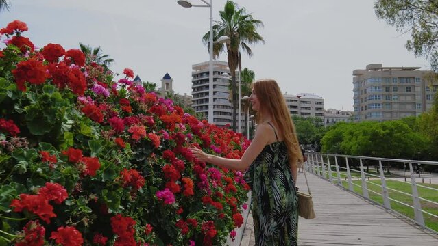 Redhead woman with a long is waking on a bridge with red flowers.