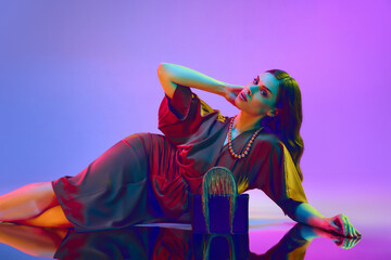 Beautiful sexy woman, model lies on the floor over purple neon background. Girl wearing gentle red...