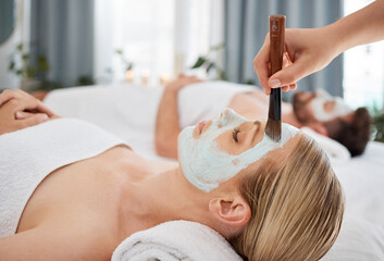 Hand, brush and mask with a couple in a spa to relax on a massage table at a luxury resort...