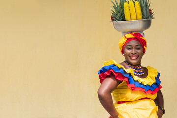 Happy, smiling fresh fruit street vendor aka Palenquera in the Old Town of Cartagena, Colombia. Afro-Colombian woman in traditional clothing, Colombian culture and lifestyle. - 608192333