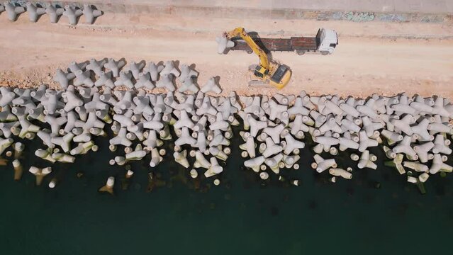 An excavator diligently constructs a dock or breakwater in the sea, its mighty arm reaching out from the shore, creating a resilient structure amidst the waves. Aerial view