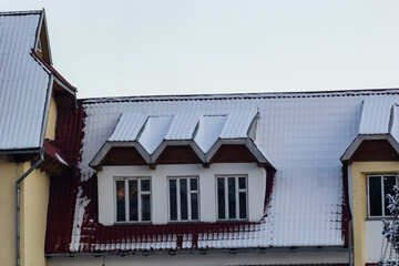 Snow on the roof of a red, brown metal roof of a European house with a window