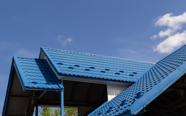 The roof of a house covered with sheets of blue metal tiles against the background of the sky on a...