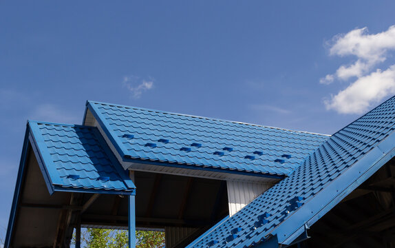 The roof of a house covered with sheets of blue metal tiles against the background of the sky on a summer day. Business selling building materials or repairing house roofs