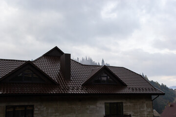 House with new brown metal tile roof and rain gutter. Metallic Guttering System, Guttering and Drainage Pipe Exterior