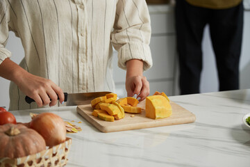 Cropped image of young woman chopping pumpkin when cooking soup for dinner