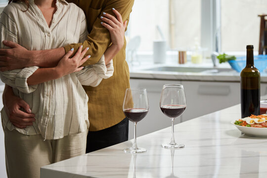Cropped image of hugging couple standing at kitchen counter with wine glasses