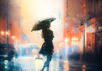 View through glass window with rain drops on blurred reflection silhouettesof a girl in walking on a rain under umbrellas and bokeh city lights, night street scene. Focus on raindrops on glass	
