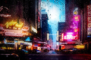 View through a glass window with raindrops on city streets with cars in the rain, bokeh of colorful city lights, night street scene. Focus on ra