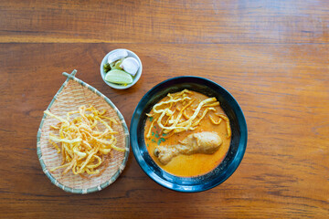 Khao Soi or Kao Soi Thai Curry Soup Noodles with Chicken and Thai spicy egg noodles on a wooden table. The delicious favorite famous Thai Food.