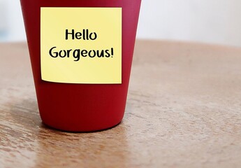 Yellow note stick on red cup on copy space background with handwriting 'Hello Gorgeous' , concept...